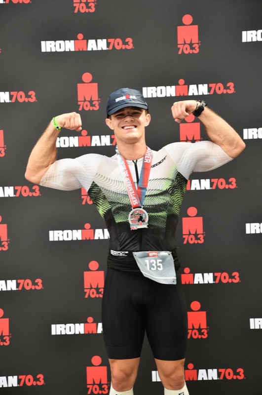 Joseph Lewand celebrating with his finisher medal at an Ironman 70.3